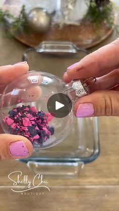 two hands holding a glass ball filled with pink and purple flowers