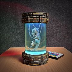 a glass jar with a lizard inside sitting on a table next to a remote control