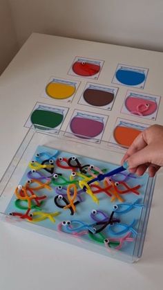 a person is holding scissors in front of an assortment of colored objects on a table