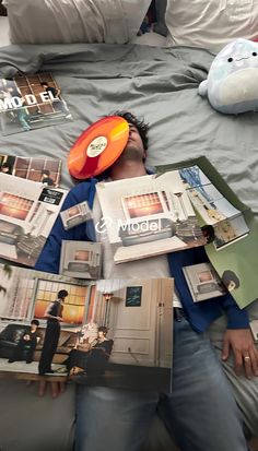 a man is laying in bed with magazines and a frisbee on his head