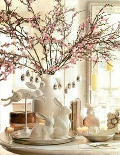 a white vase filled with pink flowers and bunny figurines on top of a table