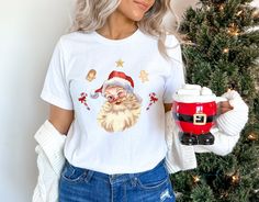 Christmas Santa Shirt, Retro Santa Shirt, Retro Christmas Shirt, Christmas Shirt For Women, Cute Xmas Gift, Santa Shirt, Gift For Christmas Welcome  Great to see you here. In ModateeCO, you can find your dream style. BLACK TEXT is used for Yellow, Heather Peach, White, Light Gray, Mint Shirts. Other colored shirts have white text. F I T ∙ & ∙ S I Z I N G :-->These Unisex T-shirts have a modern-fit. Consult the size chart in the pics for an accurate fit. -->Women's sizes are narrower than the waist. -->Sleeves are rolled up in some product pictures. They do not come rolled up on delivery. T I M E ∙ T O ∙ D E L I V E R Y : -->Processing and production time is 1-2 business days. -->Delivery time varies depending on your delivery address. -->You can choose Rush and Express options for fast del Santa Shirts Women, Santas Favorite Shirt, White Relaxed Fit T-shirt For Christmas, Mint Shirt, White Christmas T-shirt With Character Print, Pink Christmas T-shirt With Short Sleeves, Santa Shirts, Christmas Tees, Retro Christmas