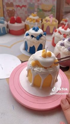 a person cutting into a cake on top of a pink plate next to other cupcakes