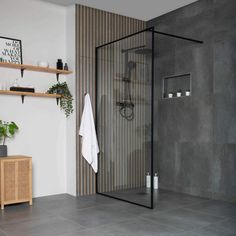 a bathroom with grey tile and wooden shelves on the wall, along with a glass shower door