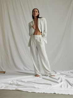 a woman standing in front of a white backdrop with her shirt open and pants rolled up