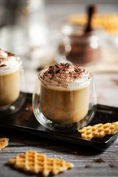 two desserts with whipped cream, chocolate and graham crackers on a black tray