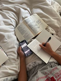 a person laying in bed with an open book and cell phone on their lap while holding a pen