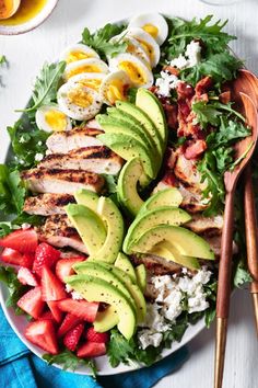 a white plate topped with chicken, strawberries and avocado next to eggs