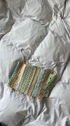 a crocheted piece of cloth on top of a white bed sheet with a string attached to it