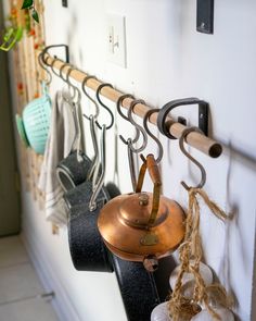 several pots and pans hanging from hooks on a white wall next to other kitchen utensils