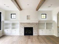 an empty living room with wood floors and white walls, built in bookshelves