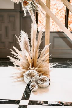 some silver balls are sitting on the floor next to a tall grass plant in front of a stair case