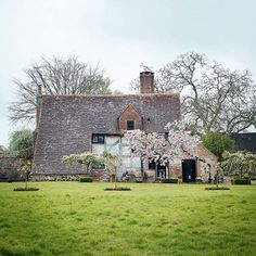 an old brick house with flowering trees in the front yard and grass lawning on both sides