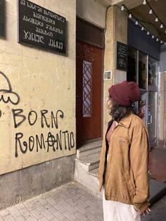 a man walking down the street in front of a building with graffiti written on it