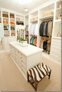 an organized closet with white cabinets and zebra print stool in the foreground, along with shelves full of clothes