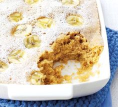 a cake with bananas and powdered sugar in a white dish on a blue towel