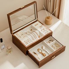 an open wooden box filled with jewelry on top of a white table next to a vase