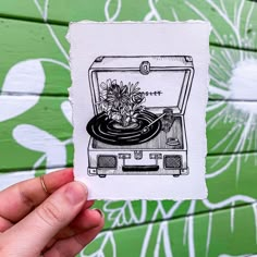 a hand holding up a piece of paper with a drawing of a record player and flowers on it