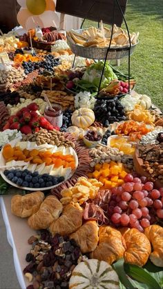 an assortment of fruits and pastries on a buffet table with balloons in the background