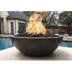 a fire pit sitting on top of a cement slab next to a swimming pool with a house in the background