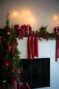 a fireplace decorated for christmas with red ribbon and candles