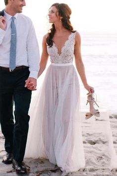 a man and woman are walking on the beach holding hands while dressed in wedding attire