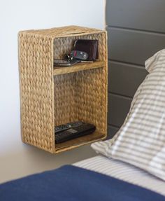 a wicker shelf next to a bed with a cell phone and remote control on it