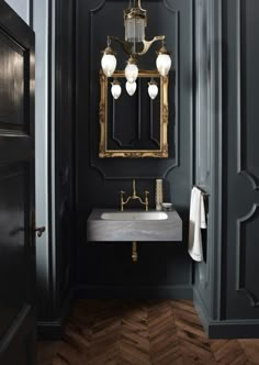 an image of a bathroom with black walls and gold accents on the mirror above the sink