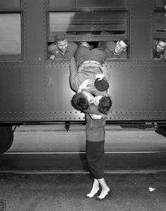 an old photo of two people standing in front of a train with their arms around each other