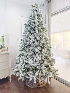 a white christmas tree sitting in a basket on top of a wooden floor next to a window