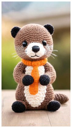 a crocheted stuffed animal is sitting on a wooden table with an orange scarf around it's neck