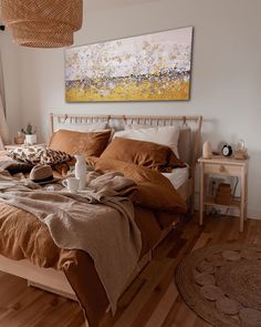 a bed with brown linens and pillows in a bedroom next to a painting on the wall