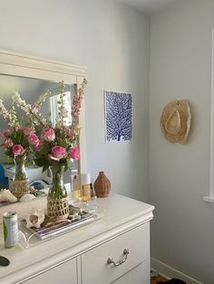 a white dresser with flowers in vases on top and other items sitting on it