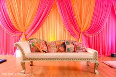 a couch with pillows on it in front of pink drapes and orange drapes