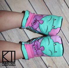 two children's shoes with pink and green cartoon characters on them, both wearing mittens