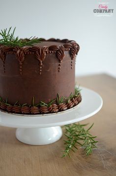 a chocolate cake sitting on top of a white plate next to a green sprig