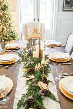 a dining room table decorated for christmas with pine cones, greenery and candles