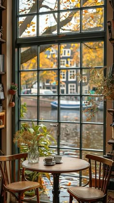 two chairs and a table in front of a window with a boat on the water