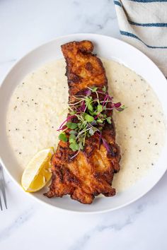 a white plate topped with fish and grits next to a lemon wedge on top of a table