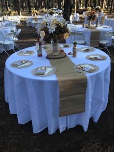 the table is set with white linens and place settings for guests to sit at