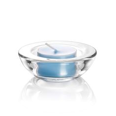 a blue candle sitting in a glass bowl on a white surface with the reflection of it's light