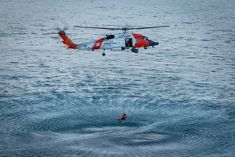 a helicopter flying over the ocean with a man standing in front of it and an object floating on the water