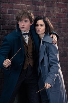 two people standing next to each other in front of a brick wall holding wands