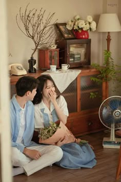 a man and woman sitting on the floor next to each other with flowers in their hands