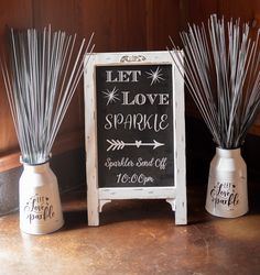 two white vases with sticks in them sitting next to a sign that says let love sparkle