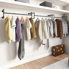 there are many sweaters hanging on the rack in this room, and one has a suit case next to it