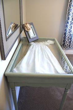 a baby's christ gown is placed on top of a glass table in front of a mirror