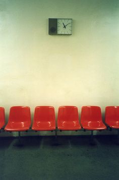 red chairs are lined up in front of a wall with a clock on the wall