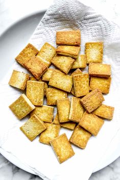 small pieces of bread are on a white plate with a napkin over it and the rest of the food is cut into cubes