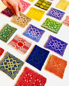 a person is pointing at some crocheted squares on a table with one hand